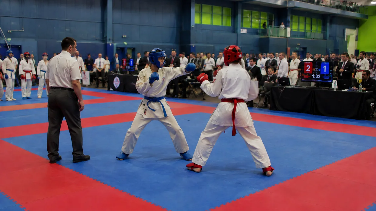 Two karate competitors mid-exchange on a competition mat, in a match being reviewed.